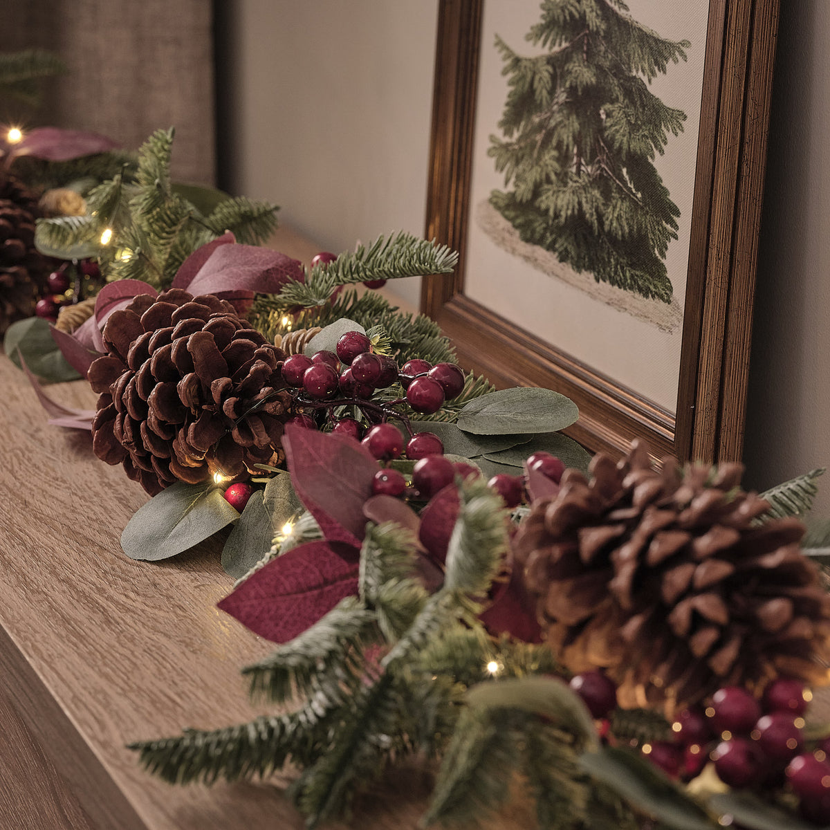 Detaillierte Ansicht der Weihnachtsgirlande mit Tannenzapfen, roten Beeren und warmweißen LEDs auf Holzfläche