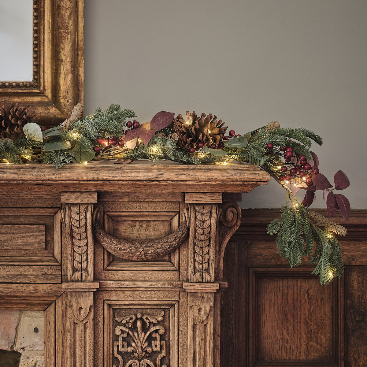 Beleuchtete Weihnachtsgirlande mit Tannenzapfen, roten Beeren und grünen Blättern auf Holzkommode