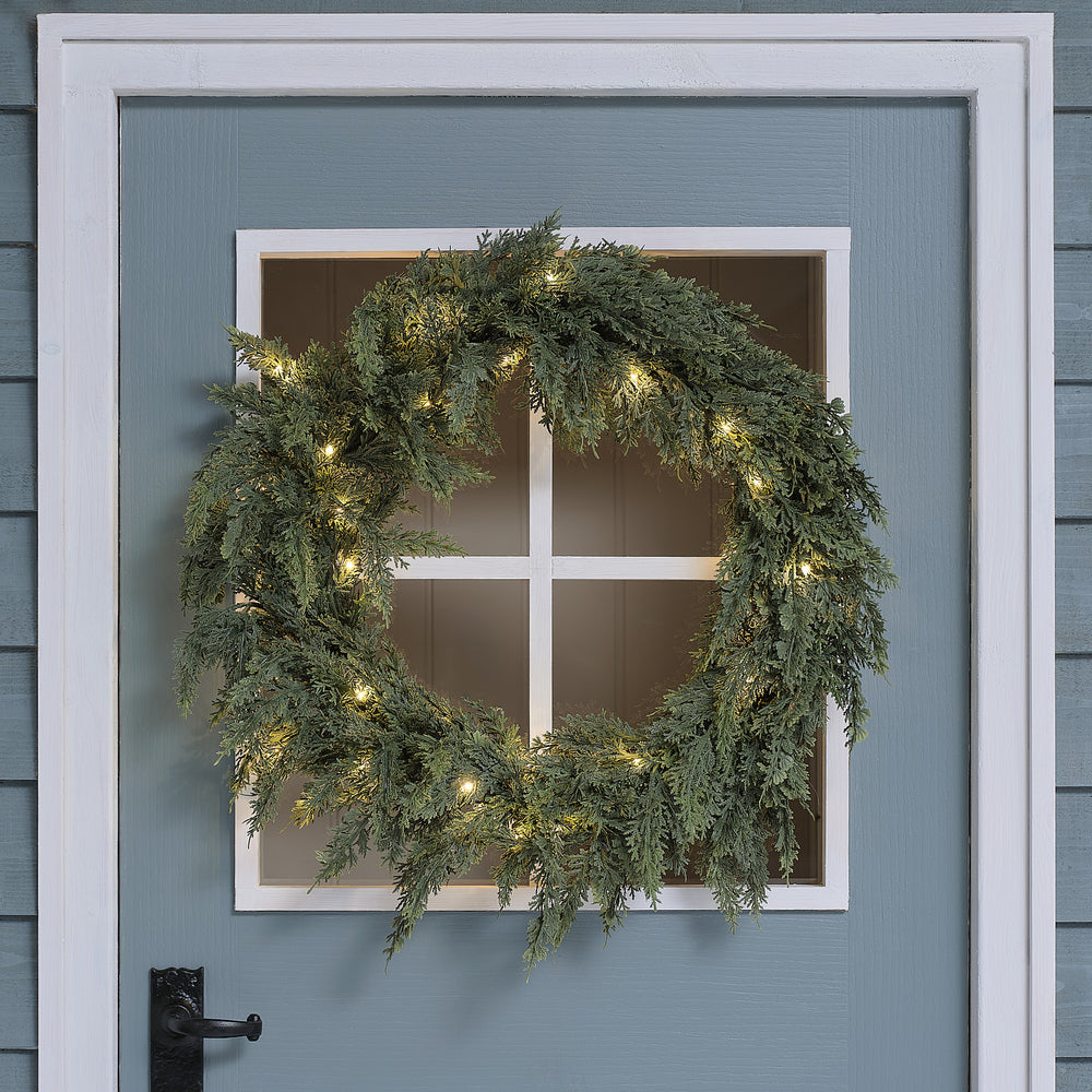 Beleuchteter Weihnachtskranz mit warmweißen LEDs an blauer Haustür mit weißem Fensterrahmen