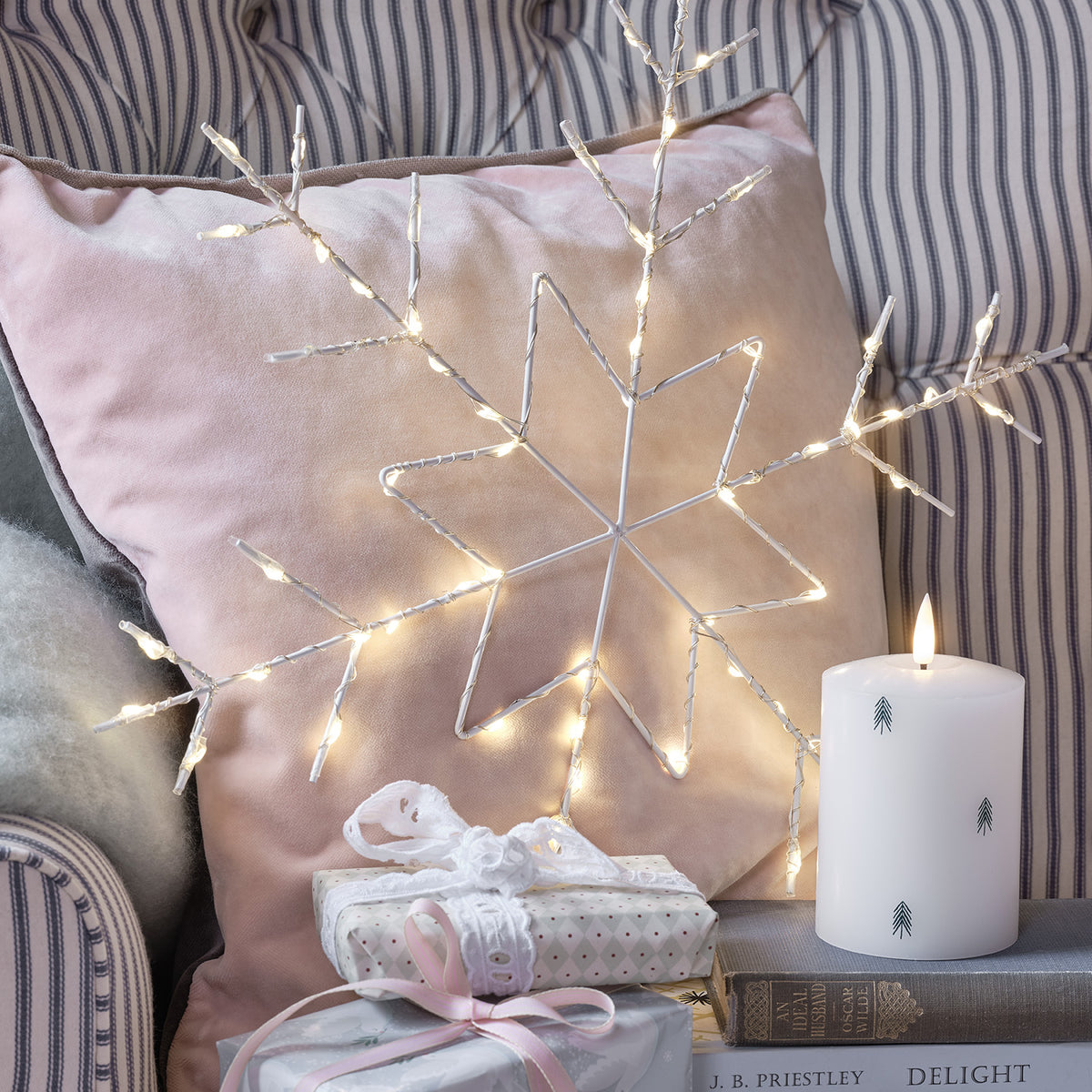 LED-Schneeflocke auf rosa Kissen neben Kerze und Geschenken auf Sofa