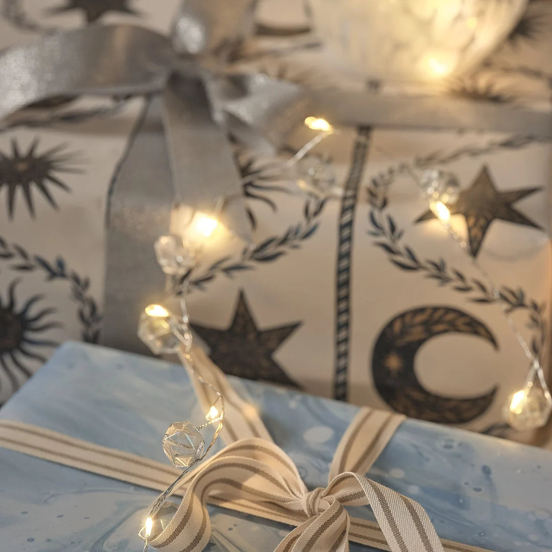 Lichterkette mit Kristallanhängern um blau verpacktes Geschenk mit Sternenmuster.
