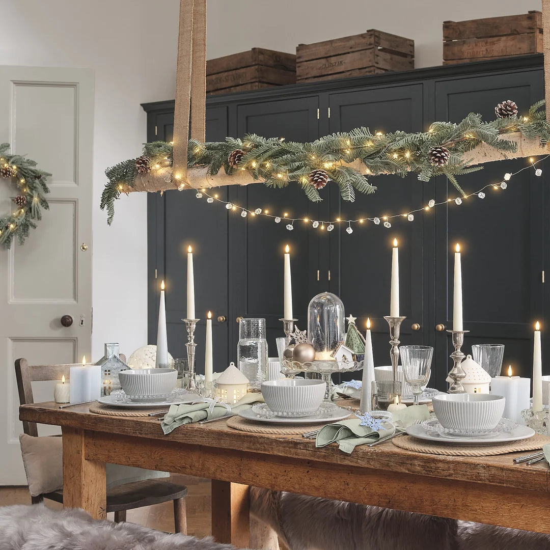 Festlich gedeckter Tisch mit Kerzen unter Girlande und Lichterkette.