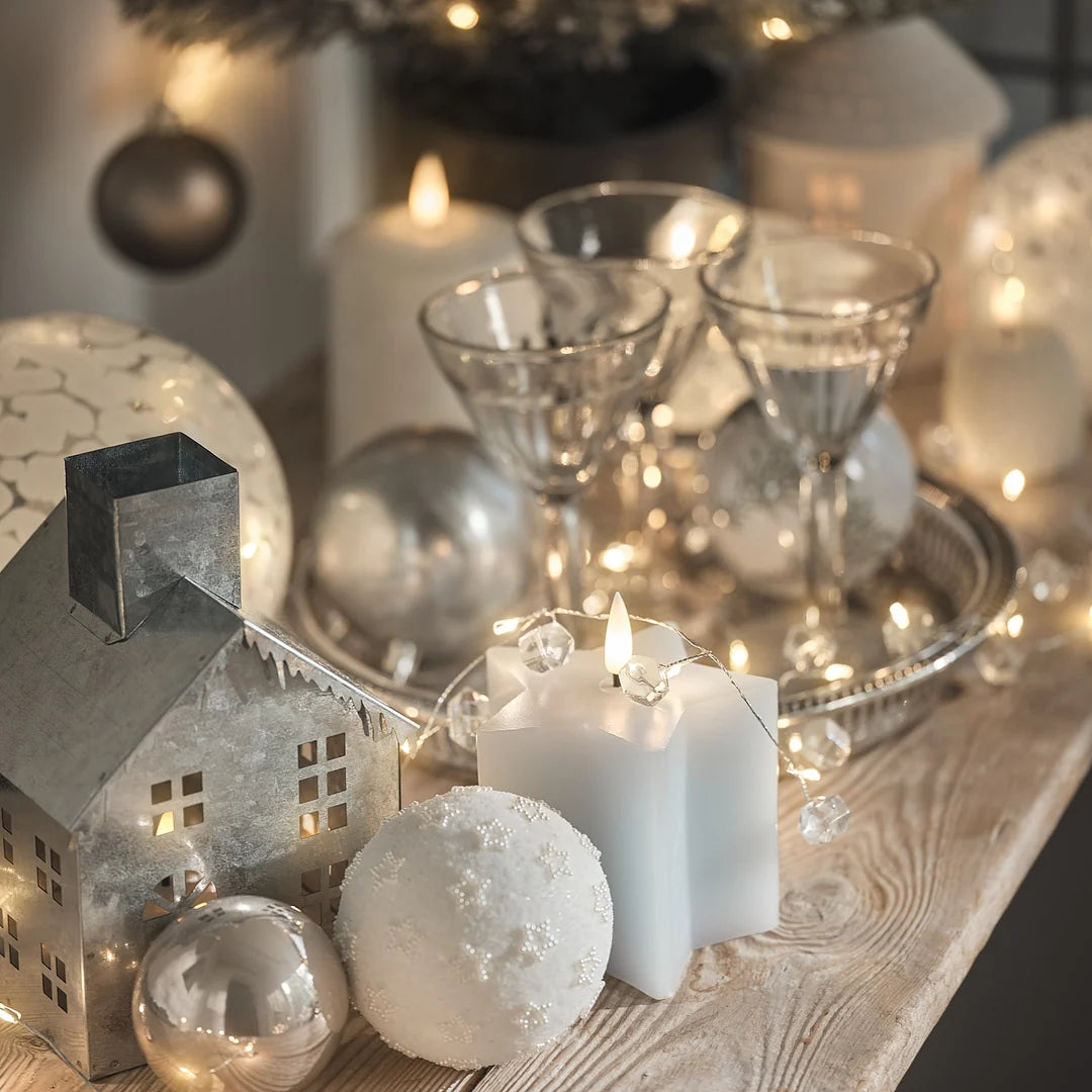 Weihnachtlich dekorierter Tisch mit Kerzen, Kugeln und Häuschenfiguren.