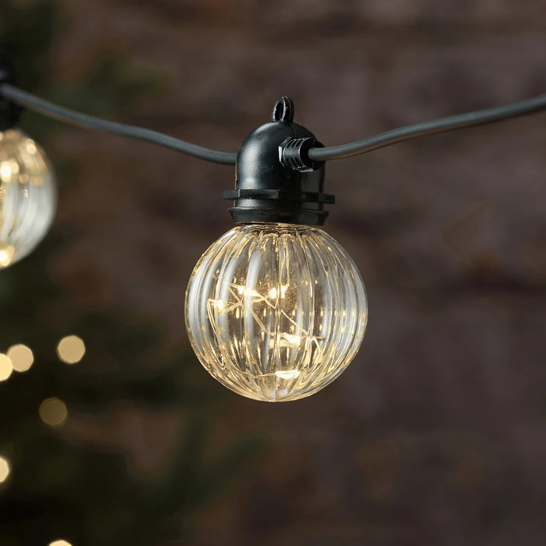 Detailansicht einer warmweißen LED-Glühbirne mit Strukturmuster vor Tannenzweig.