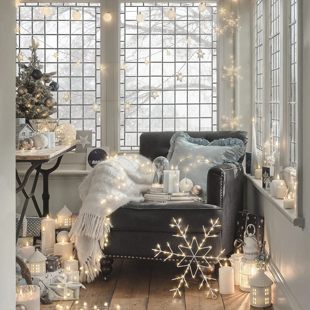 Weihnachtlich dekoriertes Wohnzimmer mit Lichterkette, Sessel und Fensterfront.