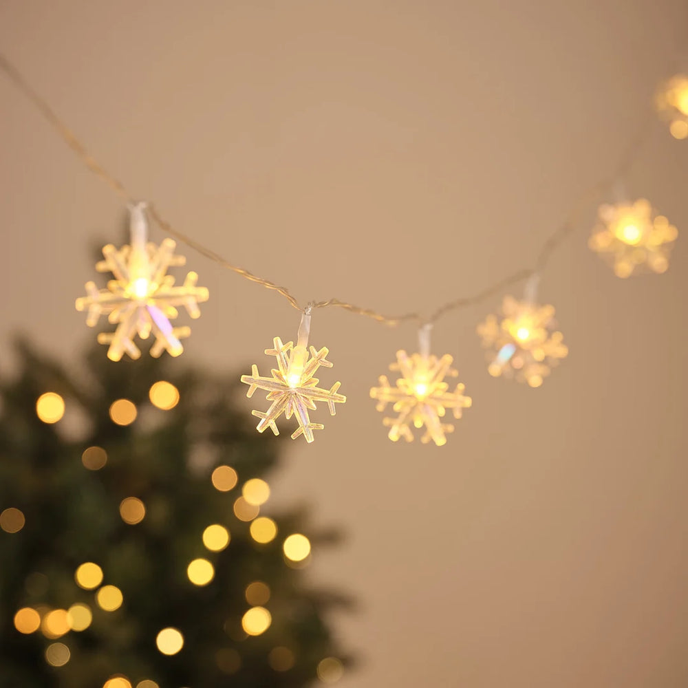 LED-Lichterkette mit leuchtenden Schneeflocken-Anhängern vor Weihnachtsbaum und Lichterglanz.