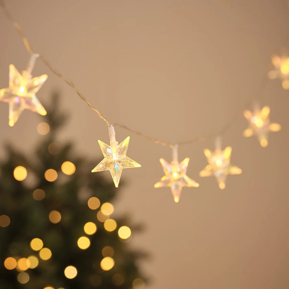 LED-Lichterkette mit irisierenden Stern-Anhängern vor Weihnachtsbaum und Lichterglanz.