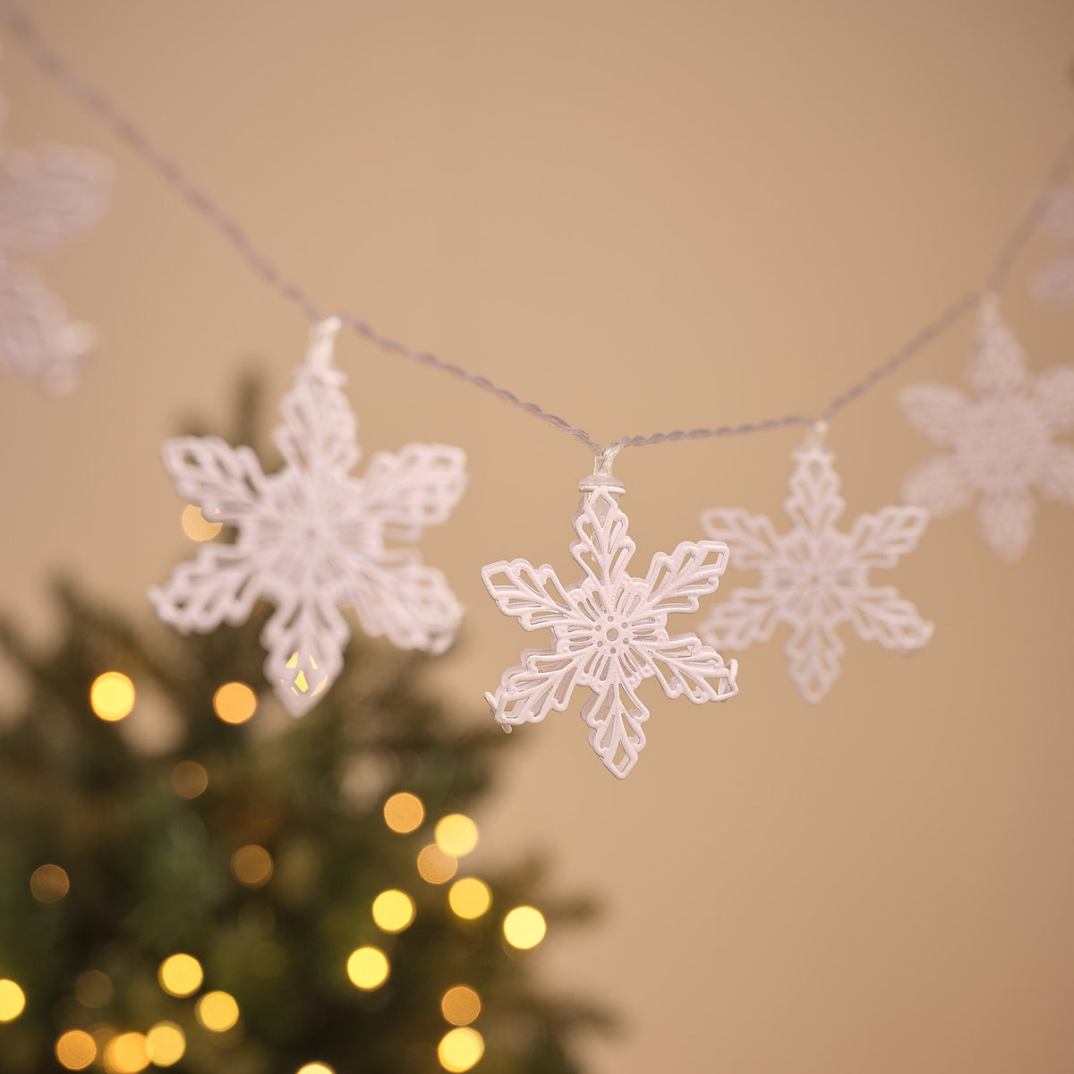 Mehrere weiße Metall-Schneeflocken mit warmweißen LEDs an transparenter Lichterkette