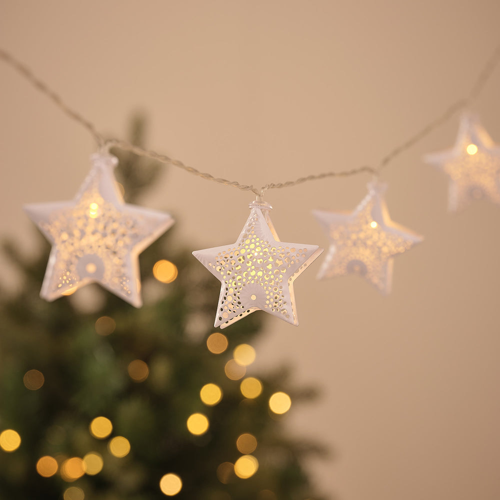 Warmweiße LED-Lichterkette mit weißen Metallsternen vor unscharfem Weihnachtsbaum