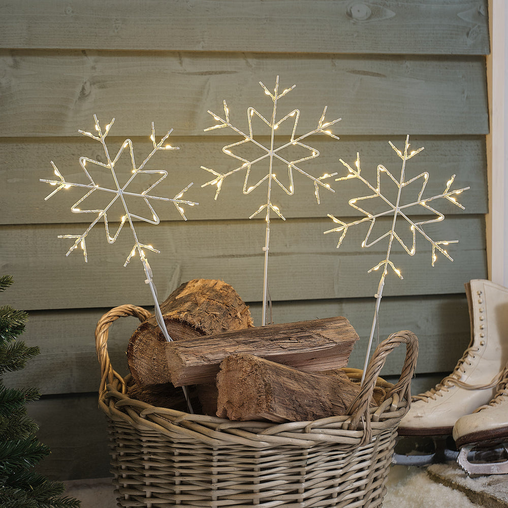 Drei weiße Schneeflocken Stableuchten mit warmweißen LEDs in einem Korb mit Holzscheiten