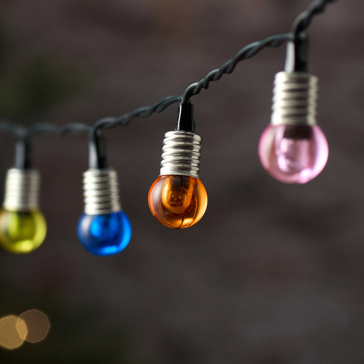 Detailaufnahme bunter LED-Kugeln mit warmweißem Licht an schwarzem Kabel