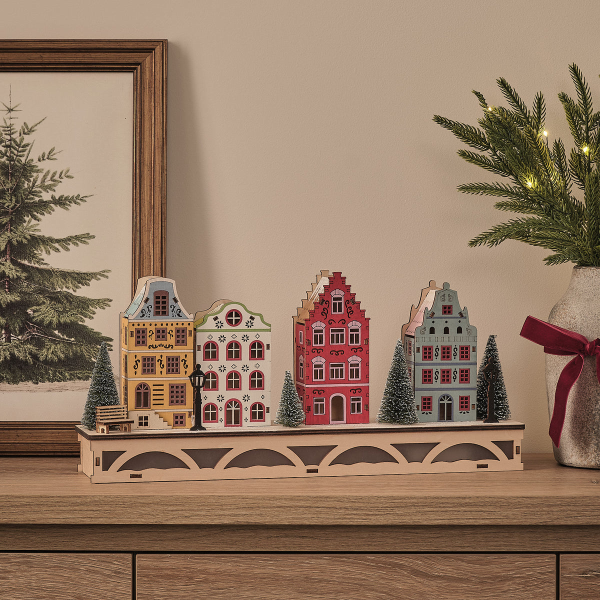 LED-Winterdorf aus Holz mit vier bunten Häuschen und schneebedeckten Bäumen ohne Beleuchtung auf Sideboard