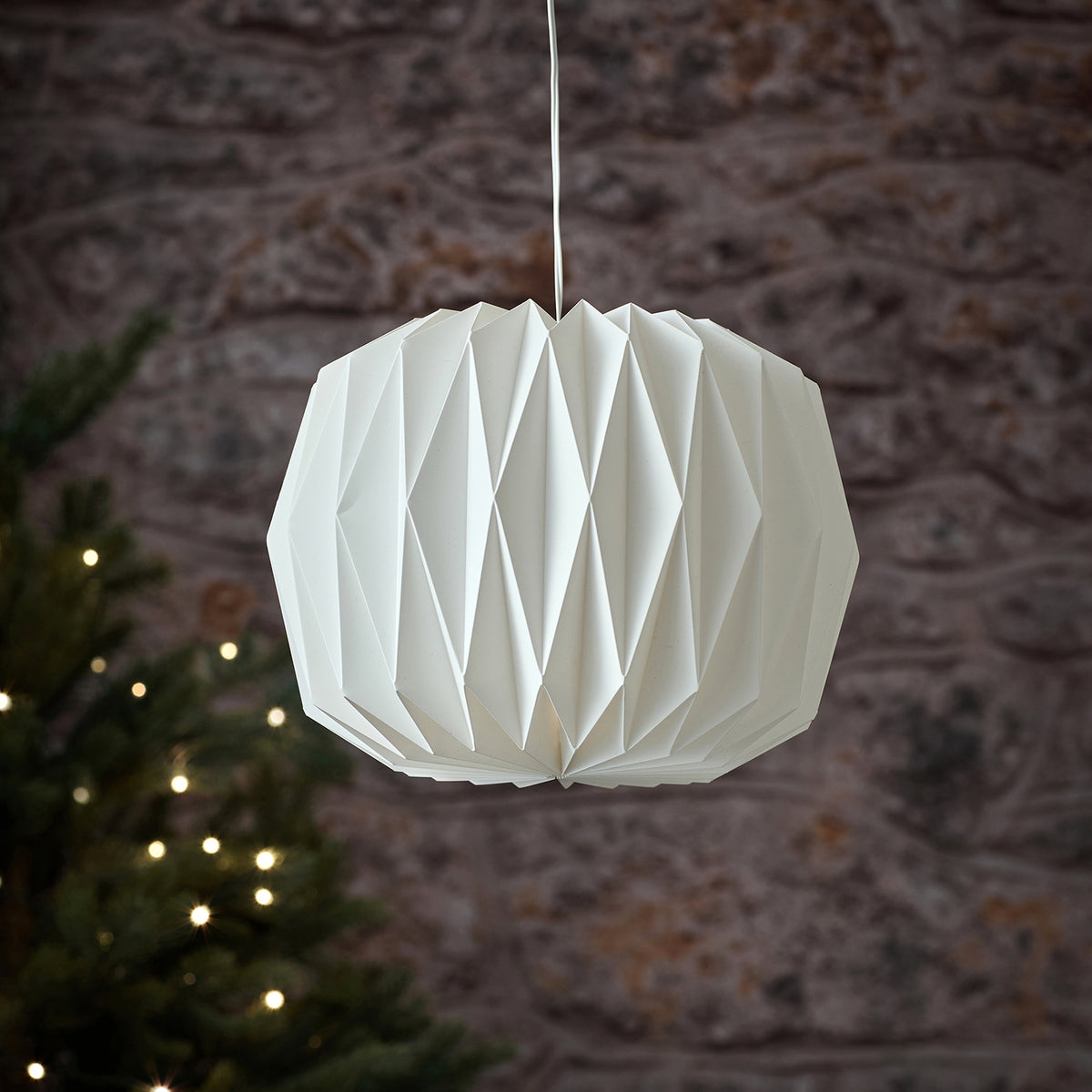 Nahaufnahme weiße LED-Papierlaterne ohne Licht vor Steinwand mit Weihnachtsbeleuchtung