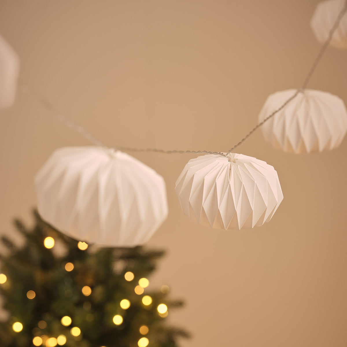 Nahaufnahme eines unbeleuchteten weißen Papierlampions mit geometrischem Faltmuster an Lichterkette