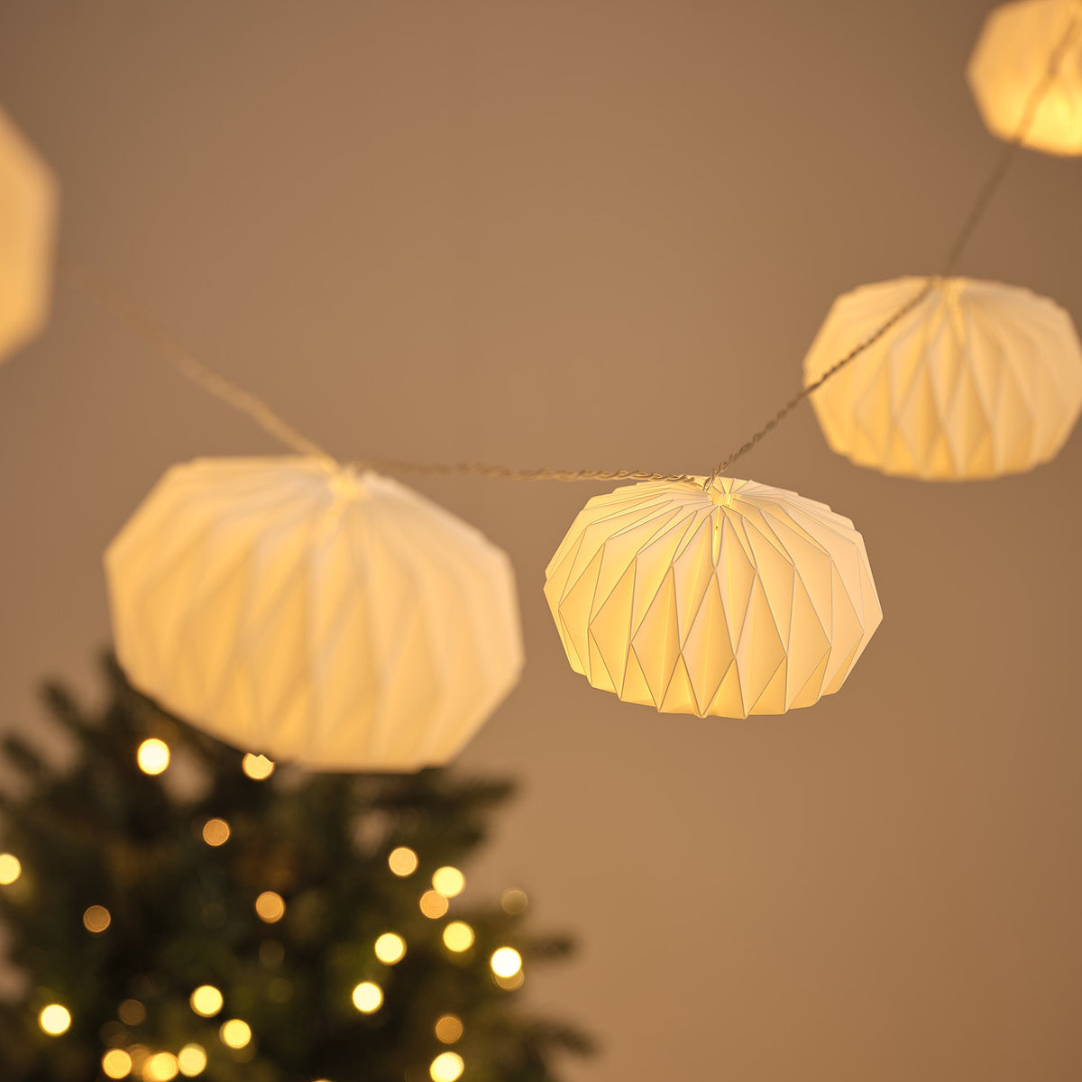 Mehrere beleuchtete weiße Papierlampions an LED-Lichterkette vor dunklem Hintergrund mit Lichterpunkten