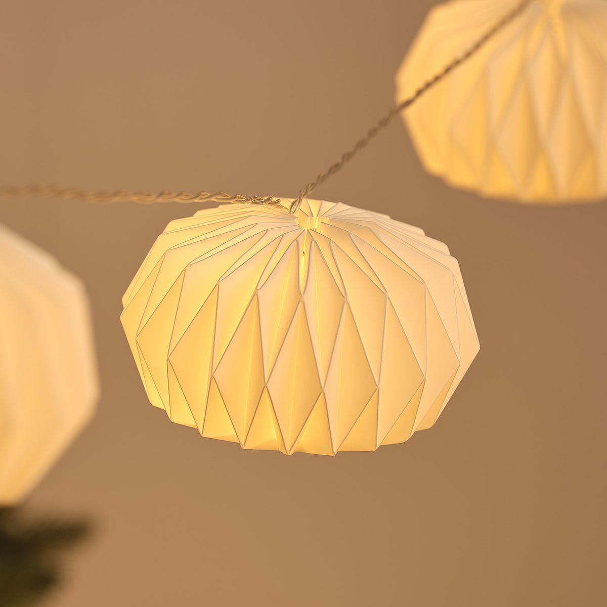 Nahaufnahme eines beleuchteten weißen Papierlampions mit filigranem Muster an transparenter LED-Lichterkette