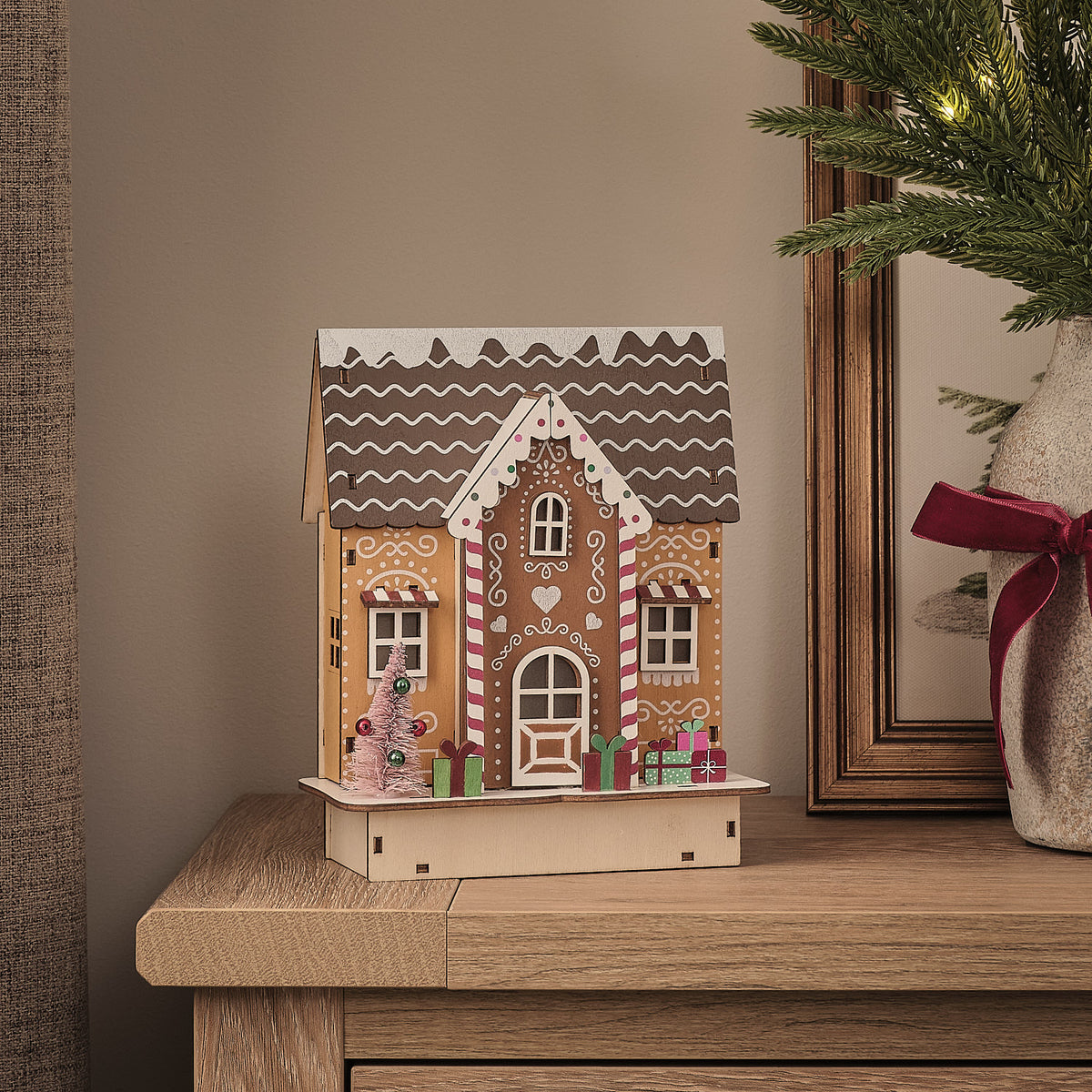 LED-Lebkuchenhaus aus Holz ohne Beleuchtung mit Weihnachtsgeschenken und kleinem Tannenbaum auf Holztisch