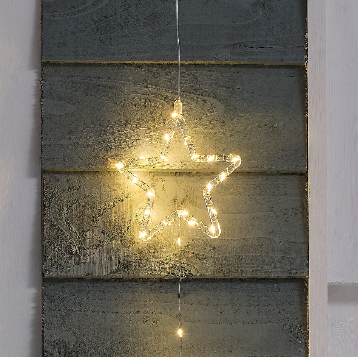 Nahaufnahme eines warmweiß leuchtenden LED-Acrylsterns mit 64 Mikro-LEDs an einer Holzfassade.