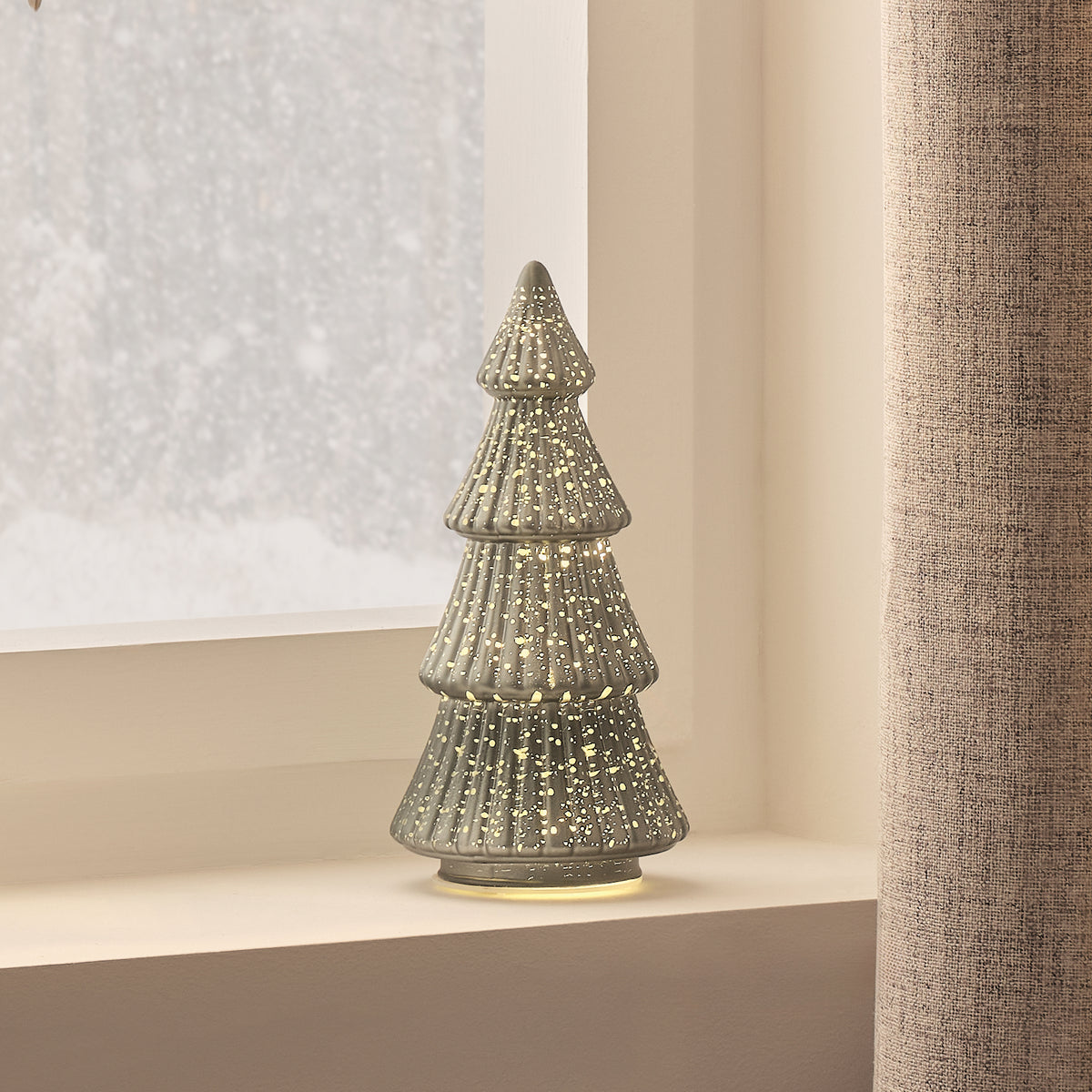 Beleuchteter LED Tannenbaum aus Glas auf Fensterbank mit beleuchtetem Papierstern