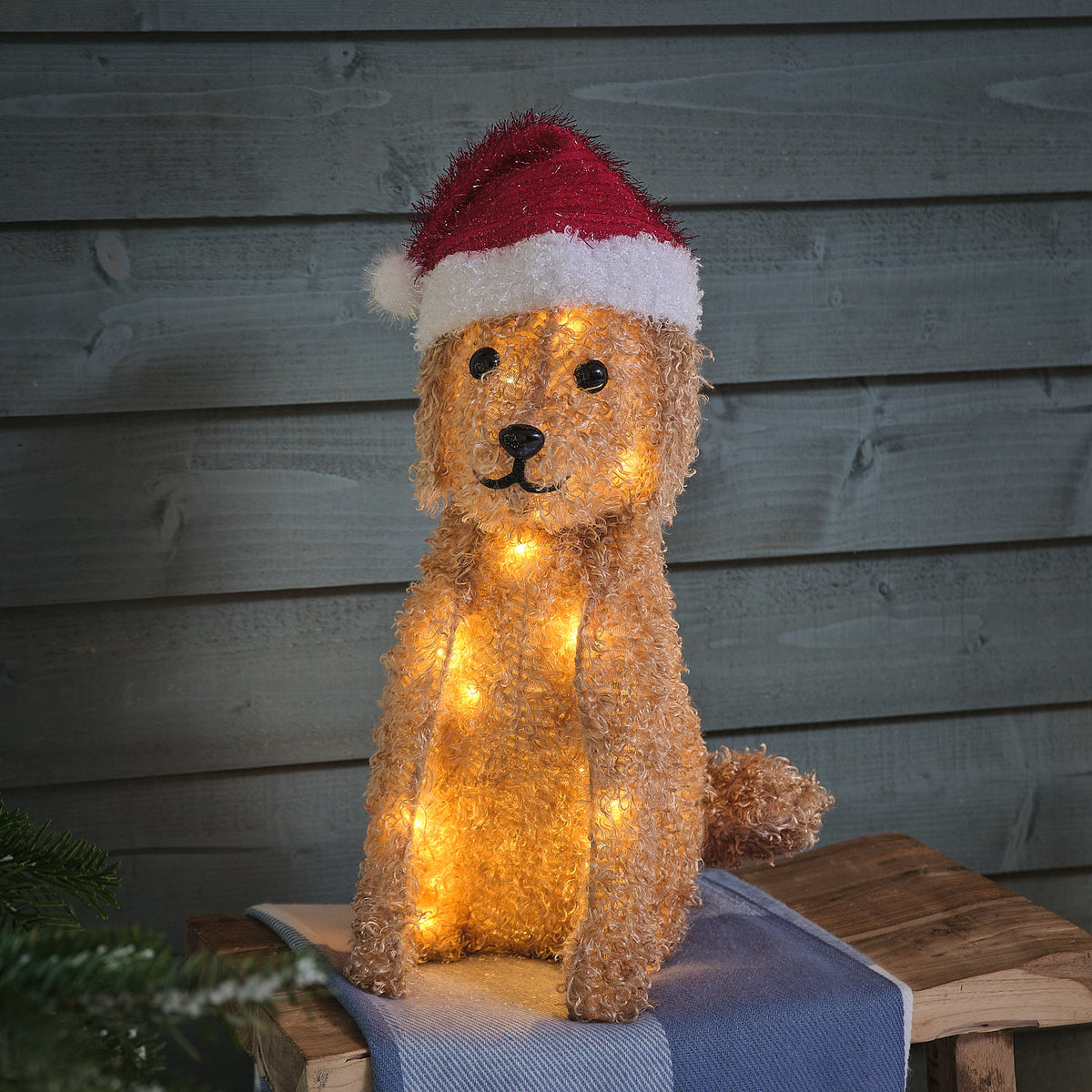 Beleuchtete LED-Weihnachtsfigur Labradoodle mit roter Weihnachtsmütze vor Holzwand