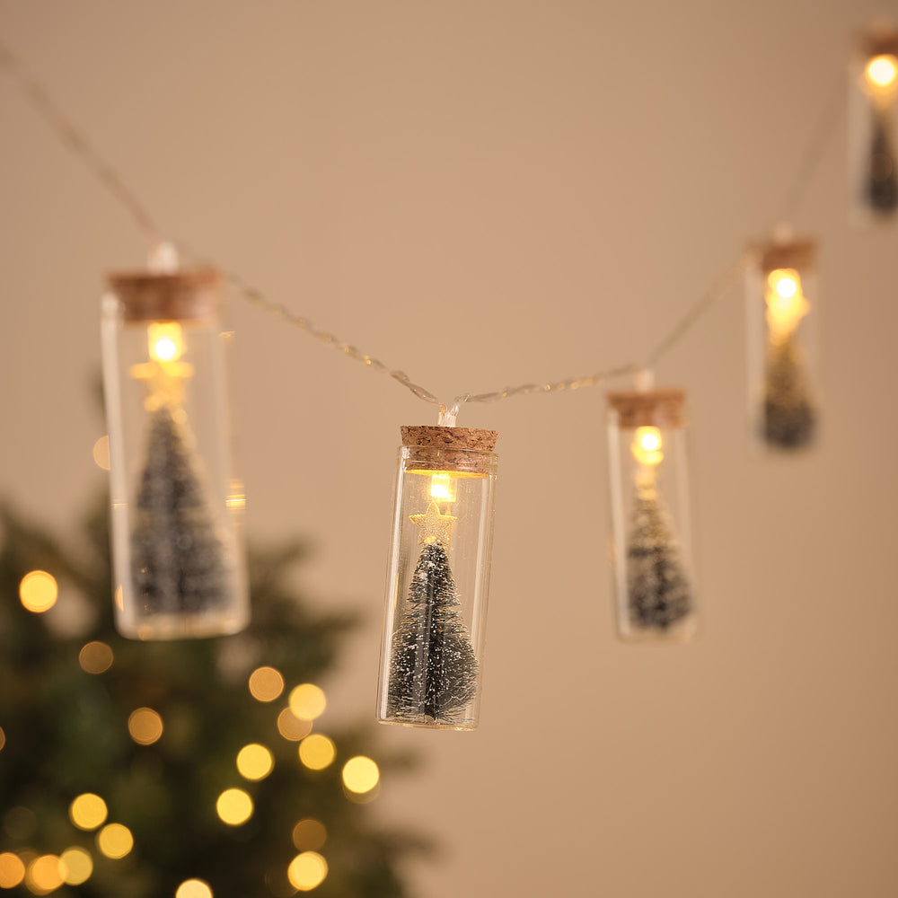 LED-Lichterkette mit Glasflaschen, jede mit schneebedecktem Tannenbaum und warmweißem Licht