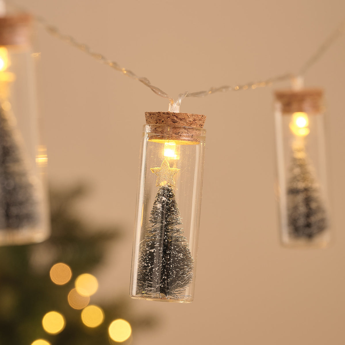 Detailansicht einer Glasflasche mit schneebedecktem Tannenbaum und warmweißer LED im Korkverschluss