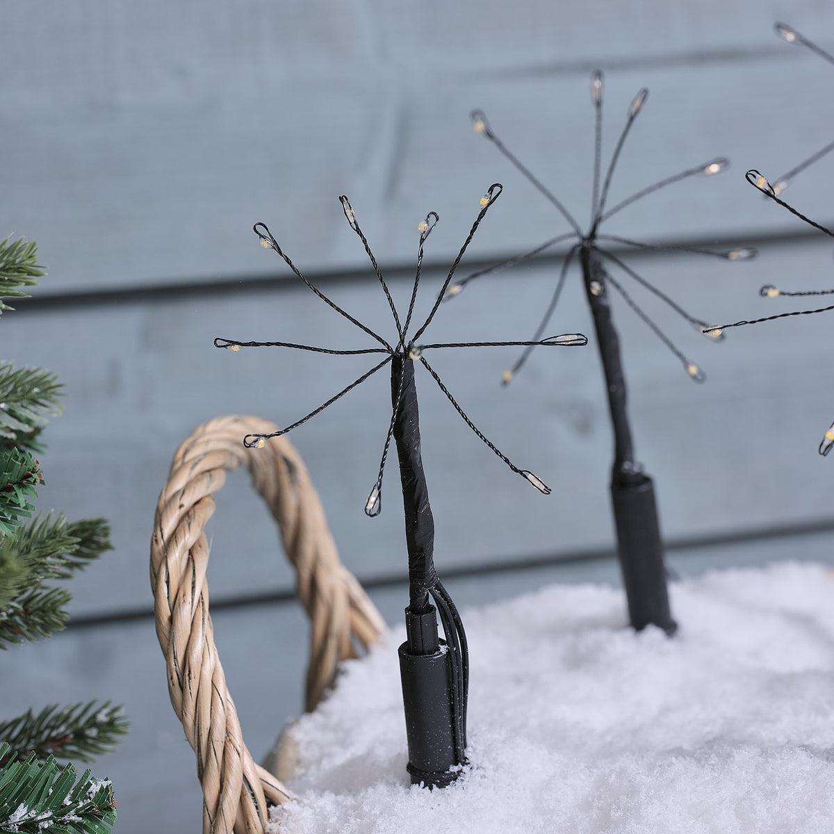 Zwei LED-Gartenstecker mit warmweißen Mikro-LEDs in einem Korb mit Kunstschnee vor blauer Wand