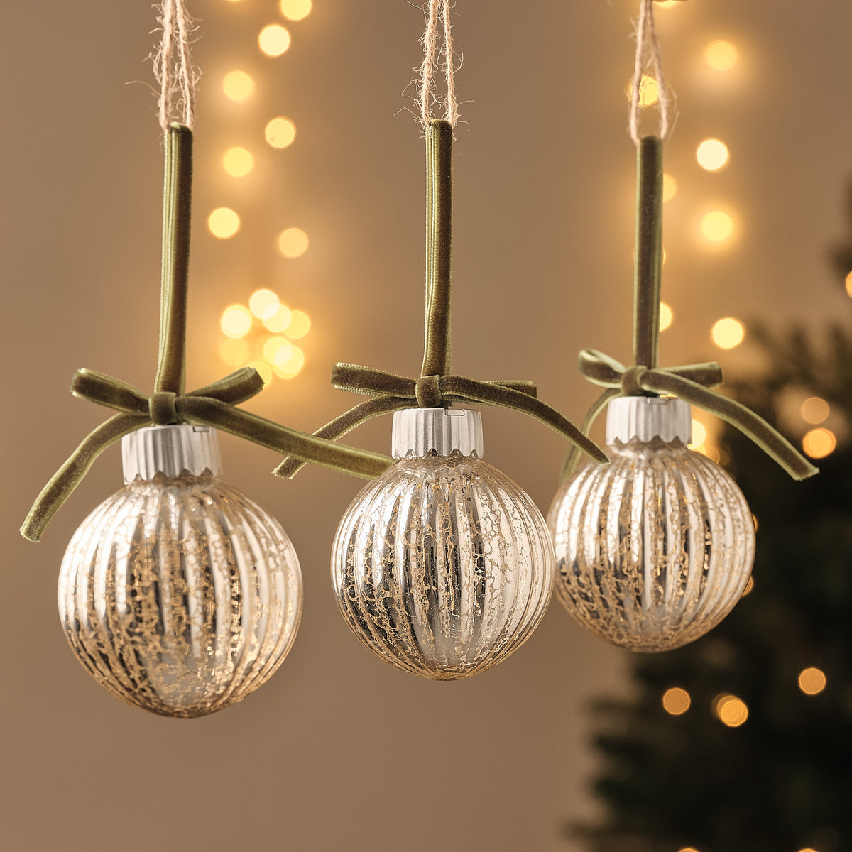 Drei LED-Weihnachtskugeln aus Glas mit grüner Schleife, warmweißes Licht, vor unscharfem Hintergrund