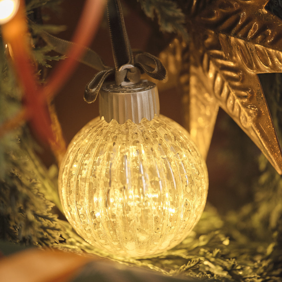 Warmweiß leuchtende LED-Christbaumkugel aus Glas mit gerippter Oberfläche und grüner Schleife am Weihnachtsbaum