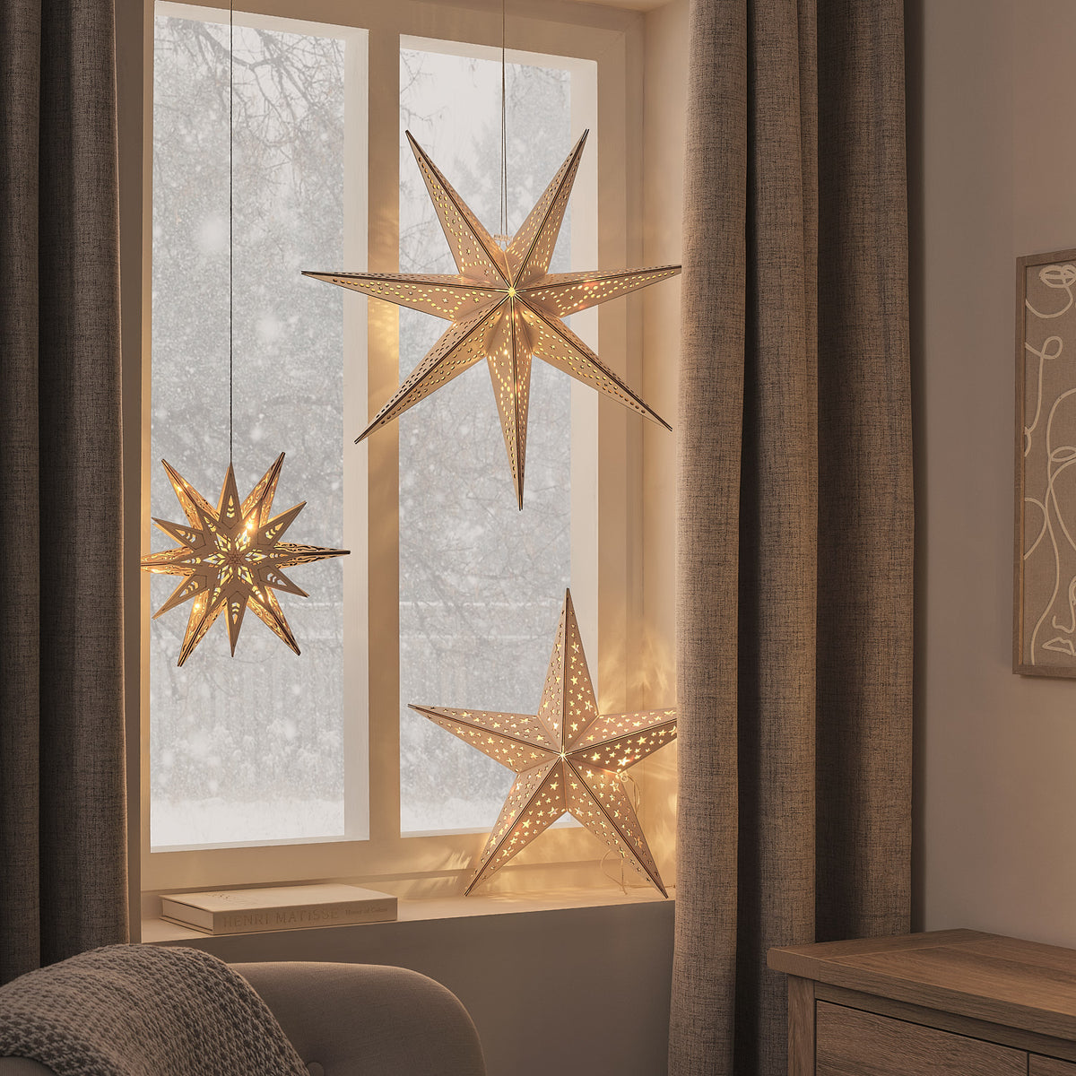 Warmweiß leuchtende LED-Holzsterne in Gold mit 5, 6 und 7 Zacken vor Fenster und Vorhängen