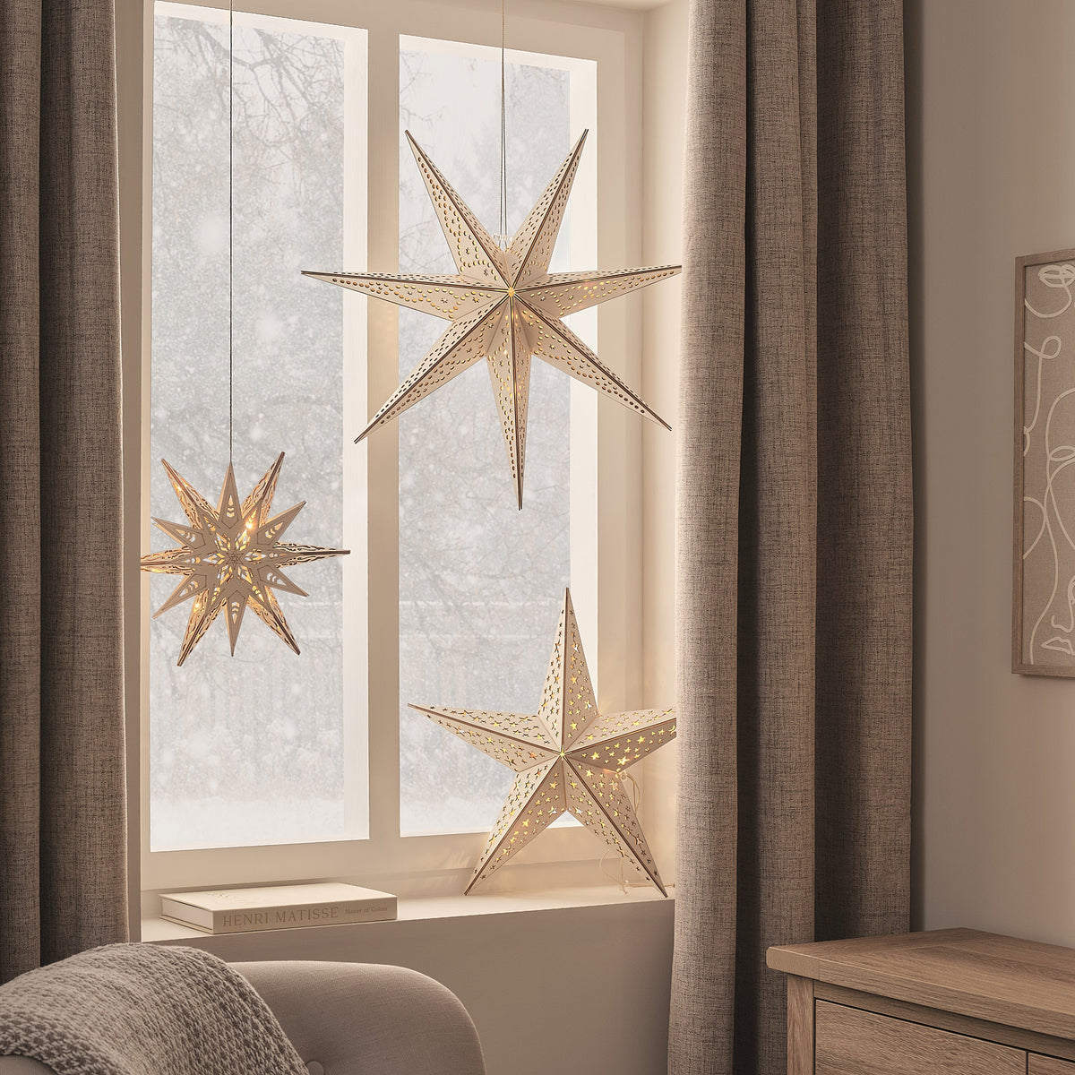 LED-Holzsterne in Gold mit warmweißem Licht hängen vor einem Fenster mit braunen Vorhängen