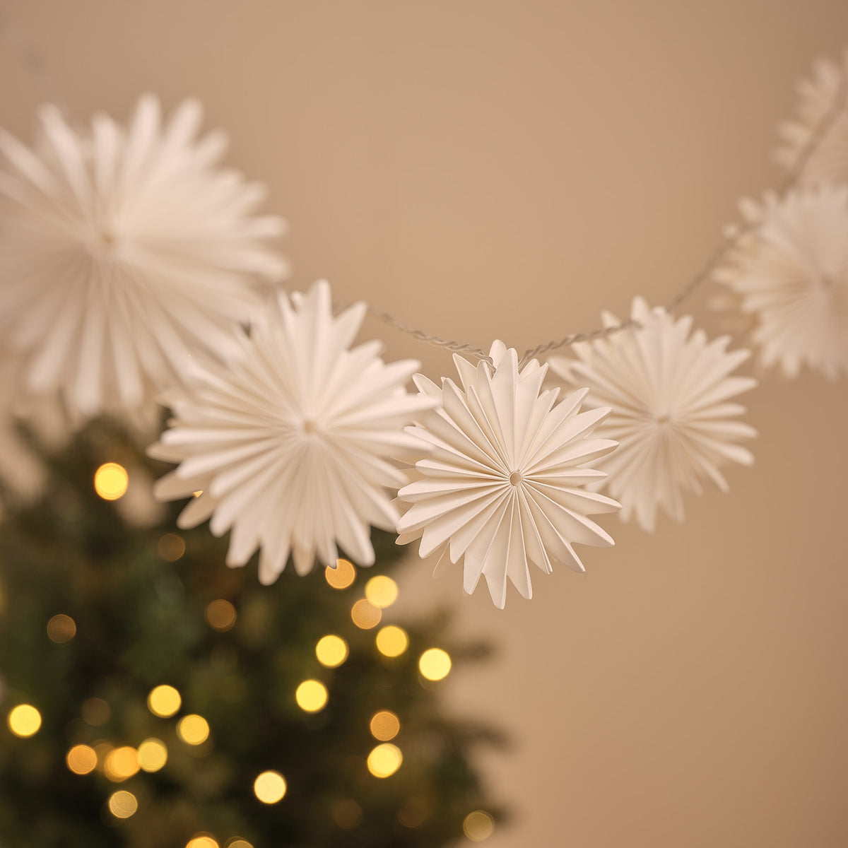 Mehrere warmweiß leuchtende Papier-Schneeflocken der LED-Lichterkette an dünnem Kabel