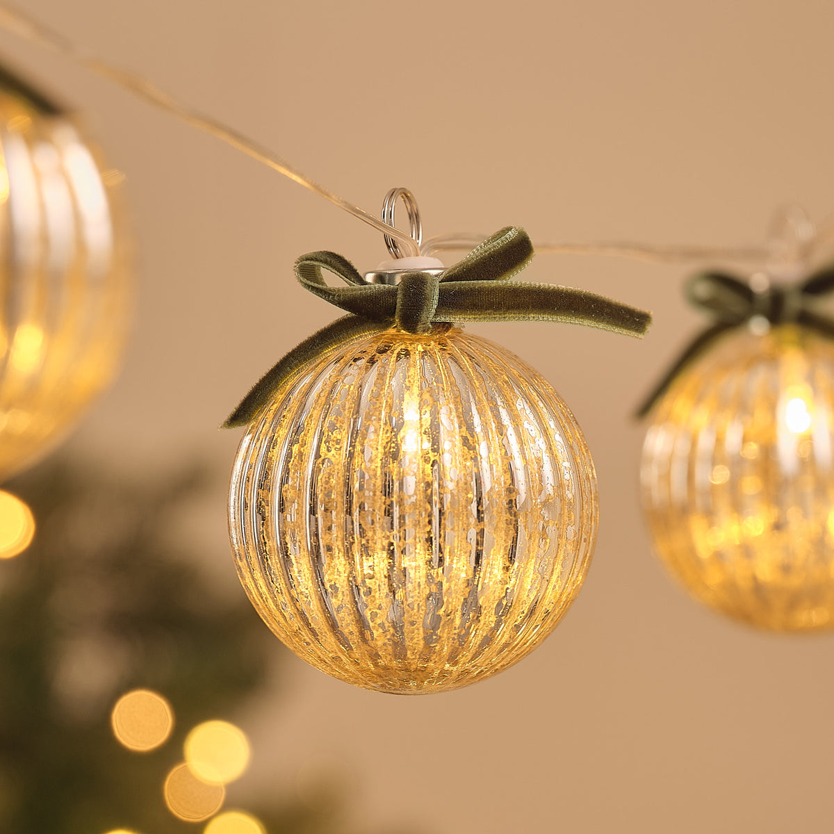 Nahaufnahme einer warmweiß leuchtenden Glaskugel mit grüner Schleife an LED-Lichterkette