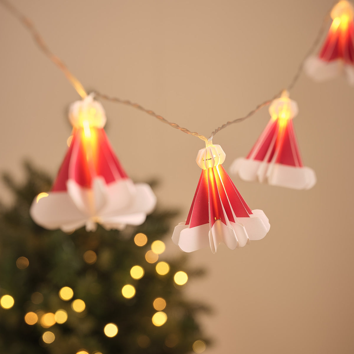 LED-Lichterkette mit zehn roten Papier-Weihnachtsmützen, warmweiß beleuchtet vor unscharfem Hintergrund