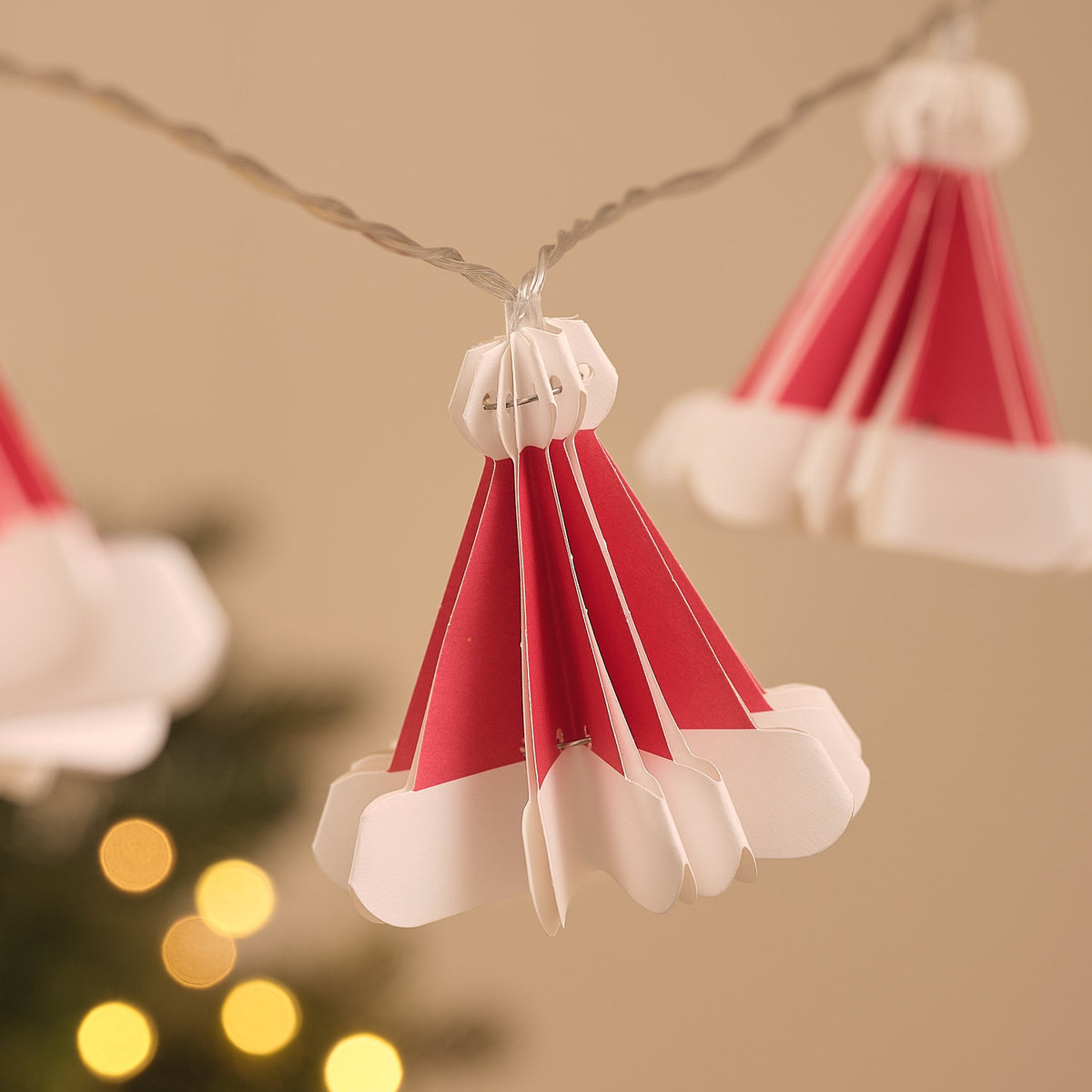Detailaufnahme einer roten Papier-Weihnachtsmütze ohne Beleuchtung an transparenter Lichterkette