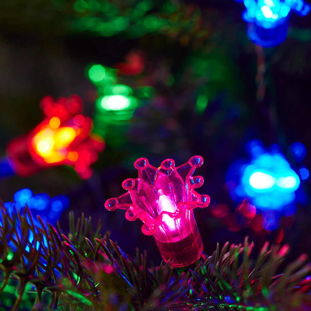 Nahaufnahme bunter LED-Sternkappen in Rot, Blau und Grün auf einem Weihnachtsbaumzweig