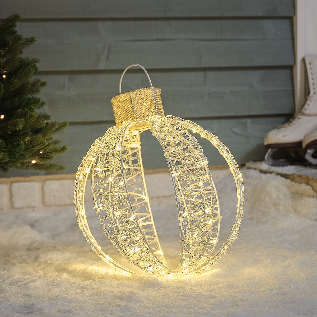 Beleuchtete LED-Weihnachtskugel mit warmweißen Lichtern auf Schnee vor Hauswand