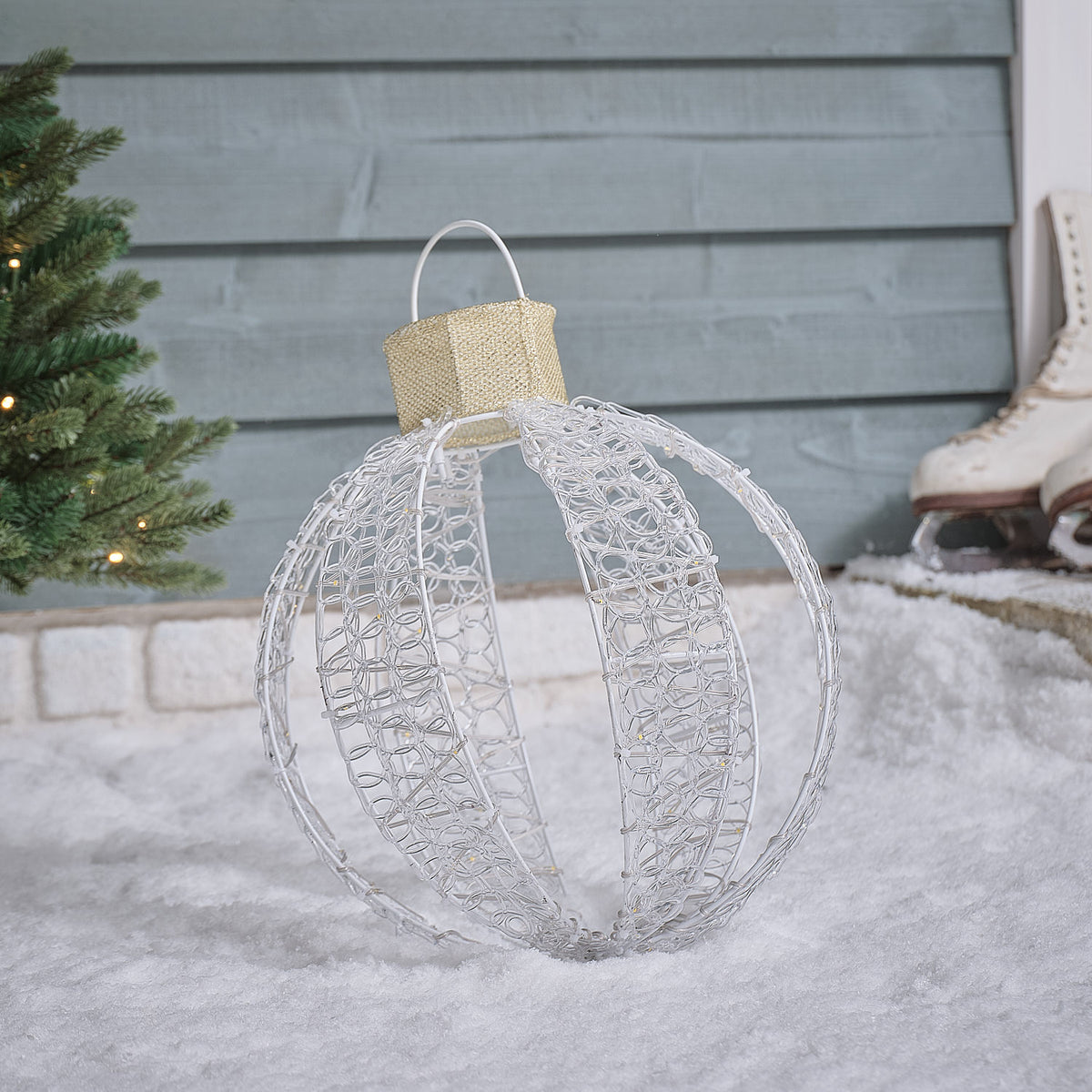 Nahaufnahme einer weißen LED-Weihnachtskugel mit goldfarbener Kappe auf weißem Gestell im Schnee