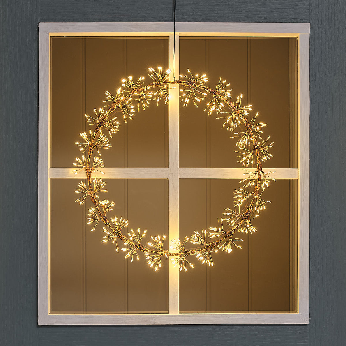 Beleuchteter LED-Starburst-Kranz außen an Fenster mit goldfarbenem Ring und warmweißen LEDs