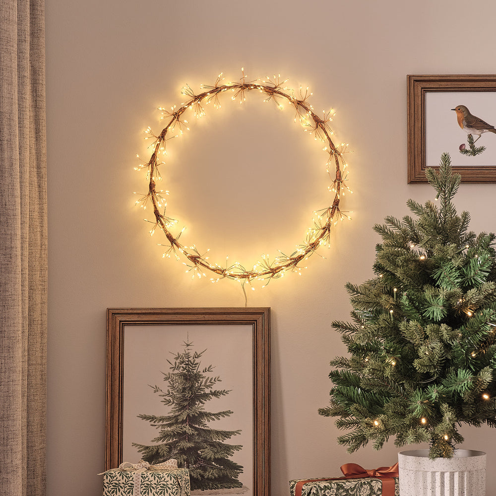 Goldfarbener LED-Starburst-Kranz mit warmweißen Mikro-LEDs an Wand über Weihnachtsbaum