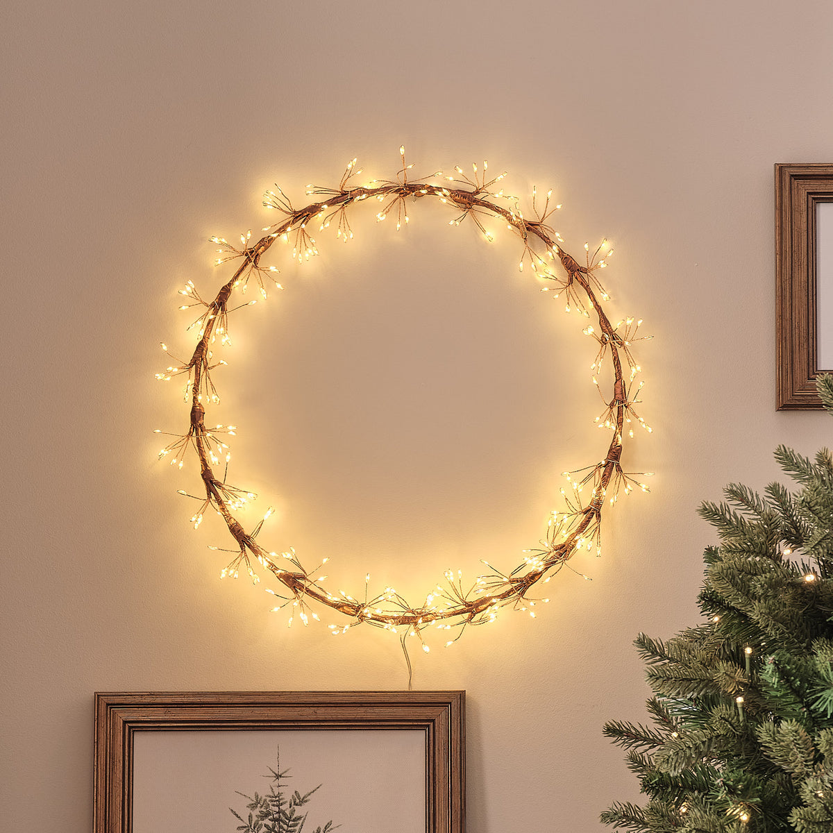 Goldfarbener LED-Starburst-Kranz mit warmweißen Mikro-LEDs an Wand über Weihnachtsbaum