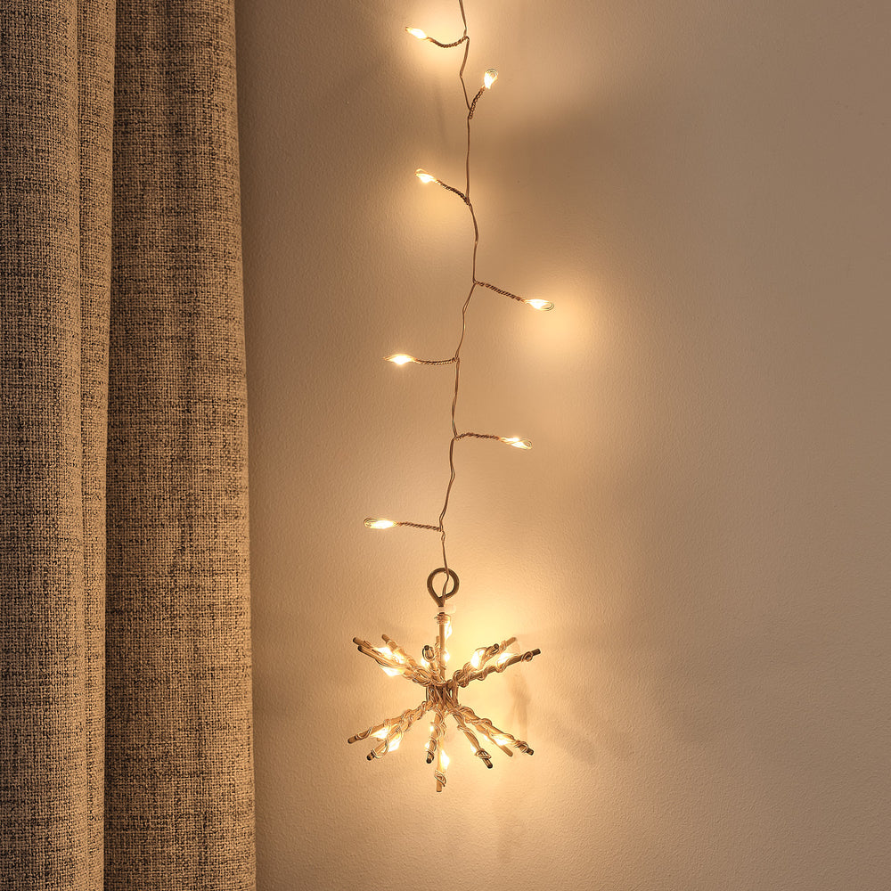 Nahaufnahme eines warmweißen LED Starburst-Clusters am goldenen Lichtervorhang vor heller Wand