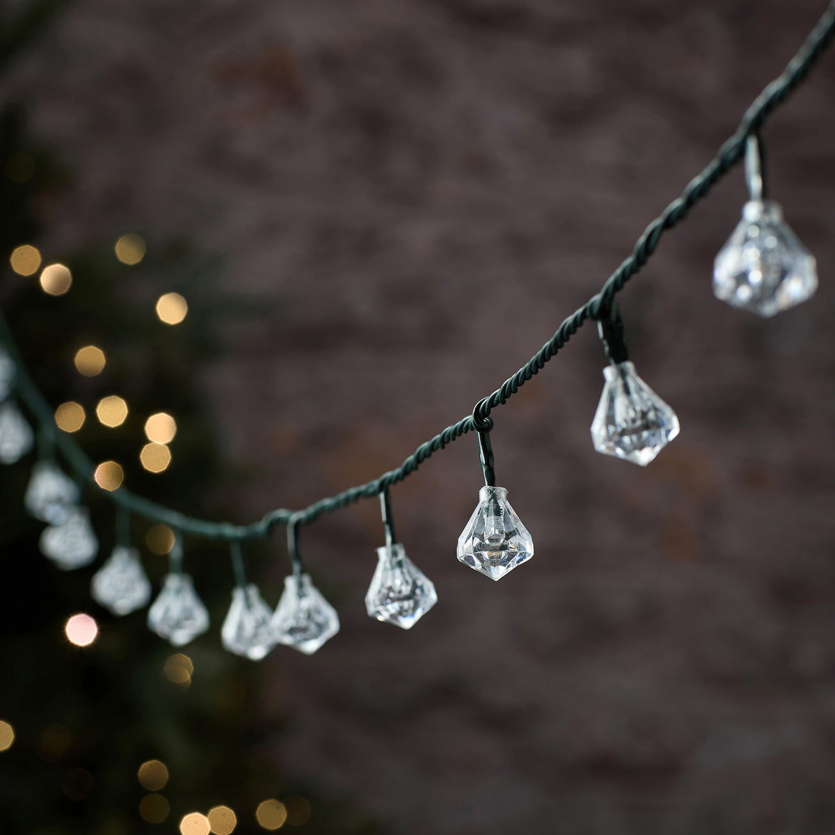 LED-Lichterkette mit transparenten Diamantkappen an grünem Kabel vor dunklem Hintergrund