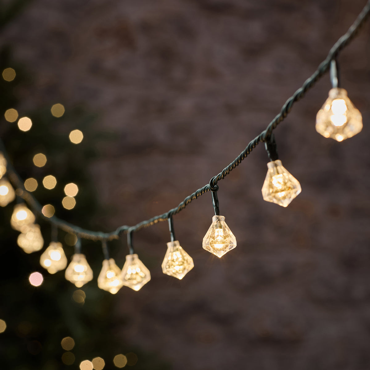 LED-Lichterkette mit warmweißen Diamantkappen an grünem Kabel vor unscharfem Hintergrund