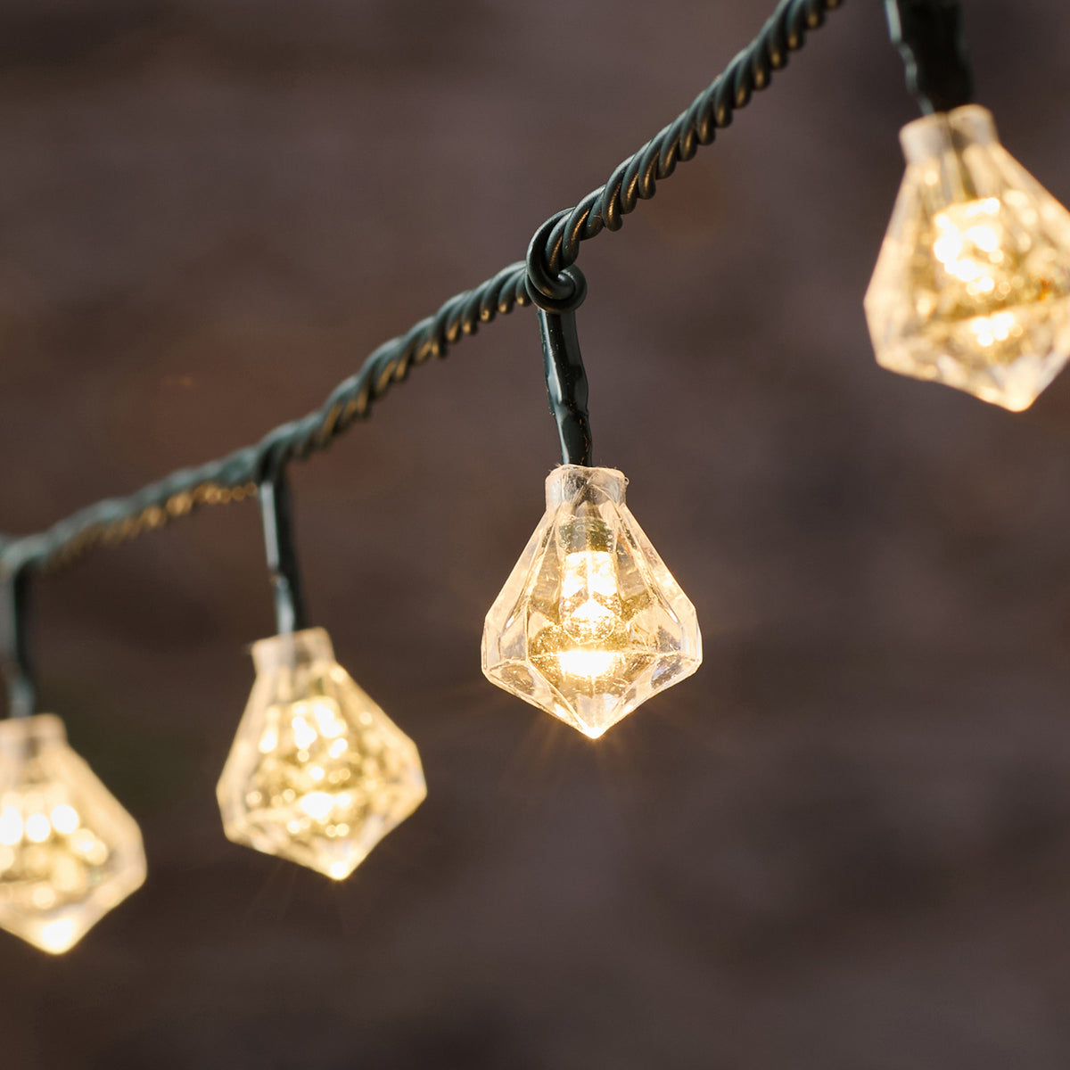 Nahaufnahme einer warmweißen LED mit facettierter Diamantkappe an grünem Kabel