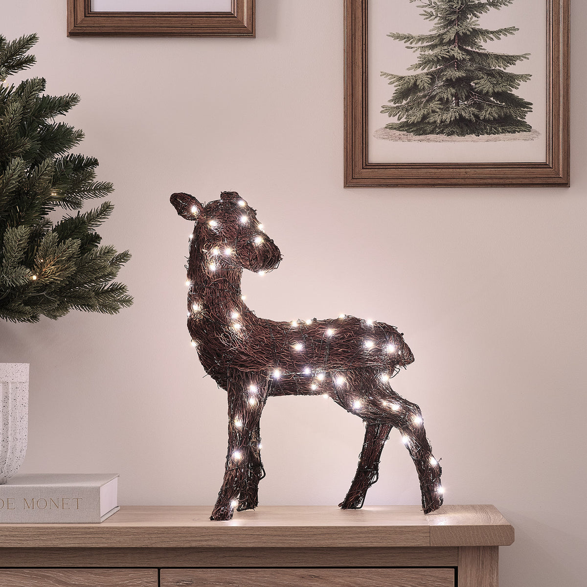 LED-Rentier aus Naturzweigen mit warmweißem Licht auf Sideboard vor Wand mit Bilderrahmen