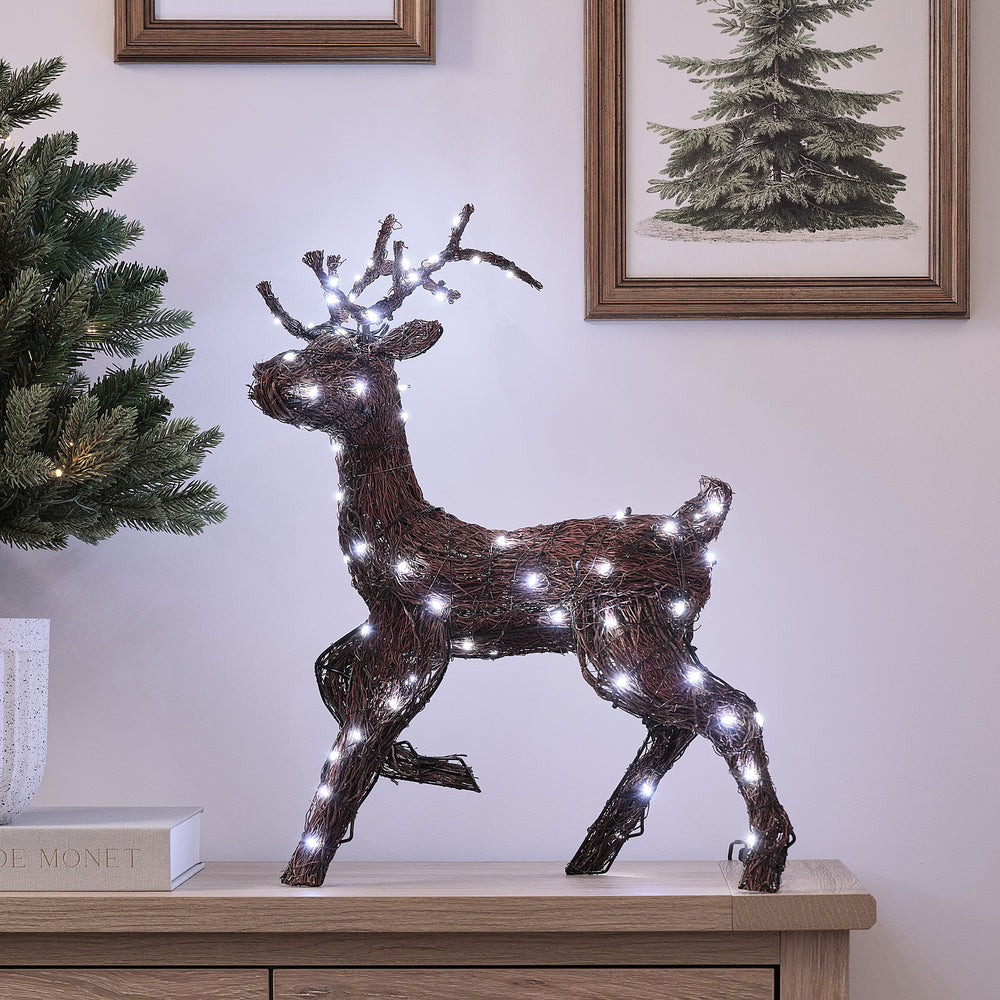 LED-Hirsch aus Naturzweigen mit kaltweiß leuchtenden Mikro-LEDs auf Kommode vor Wand mit Bilderrahmen
