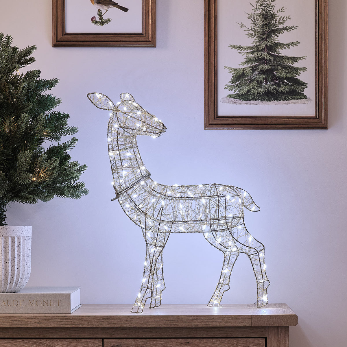 Goldene LED-Rentier-Hirschkuh mit kaltem Weißlicht auf Sideboard vor Wand mit Bildern