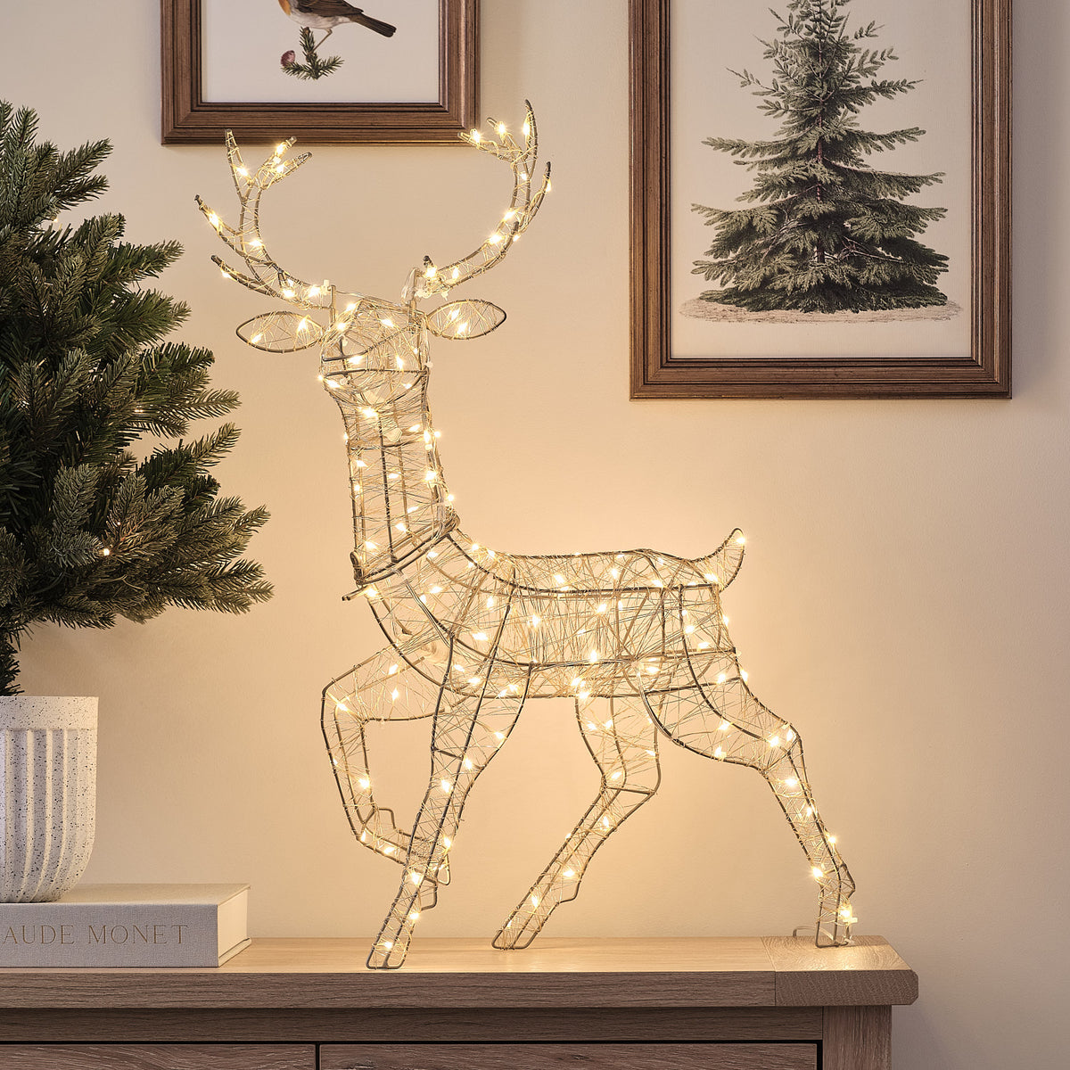 Goldene LED-Rentier-Hirschkuh mit kaltem Weißlicht auf Sideboard vor Wand mit Bildern
