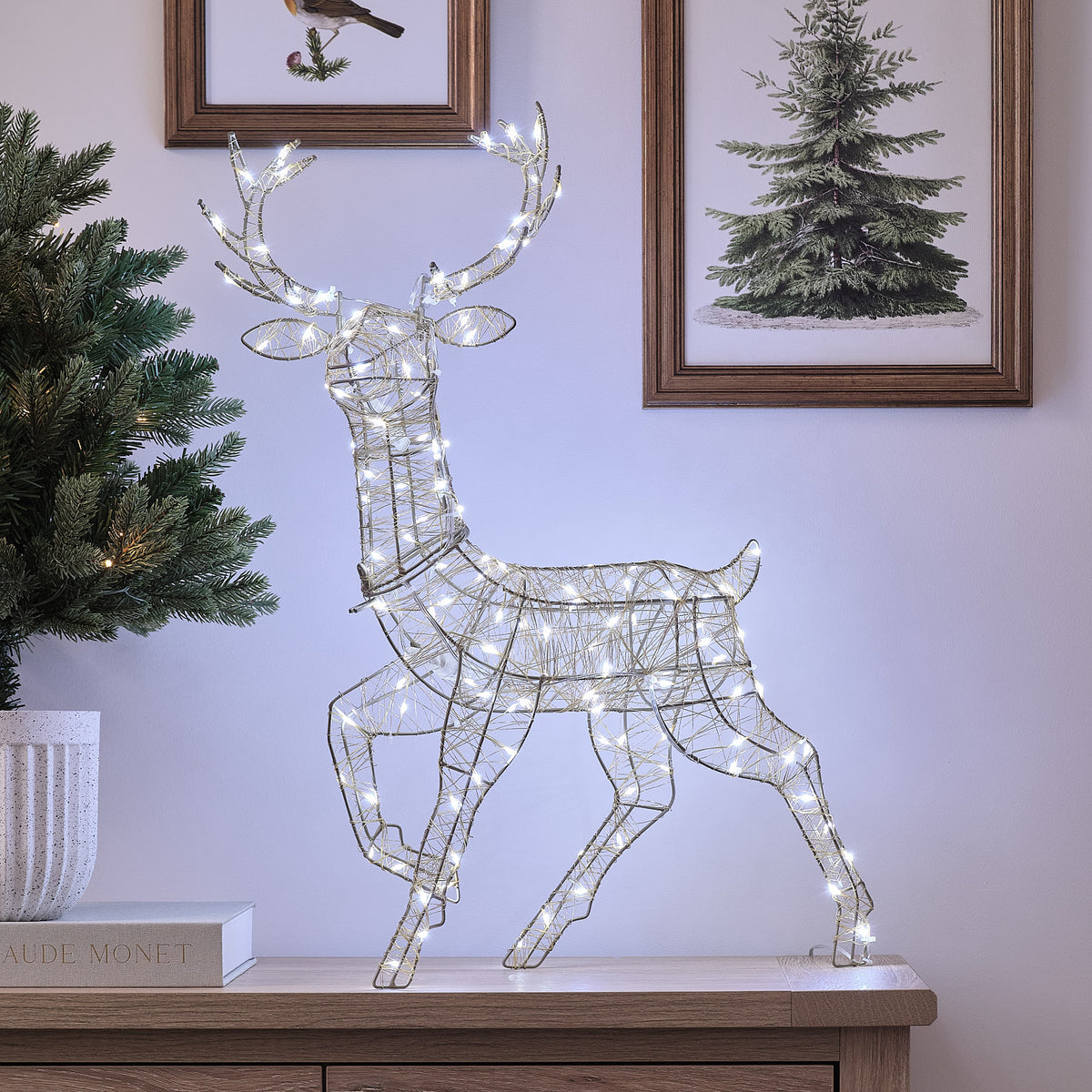 Goldene LED-Rentier-Hirschkuh mit warmweißem Licht auf Sideboard vor Wand mit Bildern